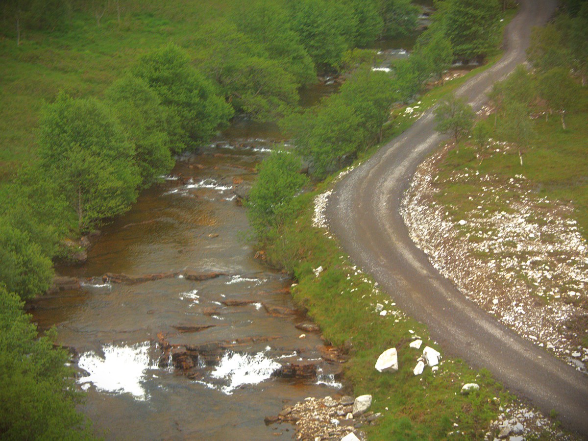 A river and a small road which exactly follows the line of the river, viewed from above and through a train window.